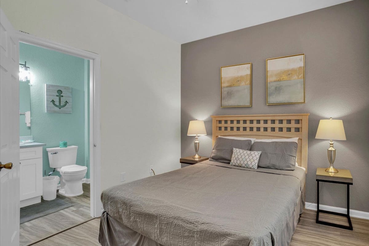 A bedroom with a bed, two bedside lamps, a headboard, and two paintings on the wall.
