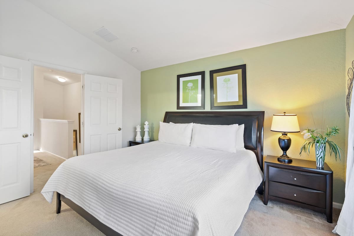 A neatly made bed with a white comforter, a nightstand with a lamp, and two framed pictures on the wall.