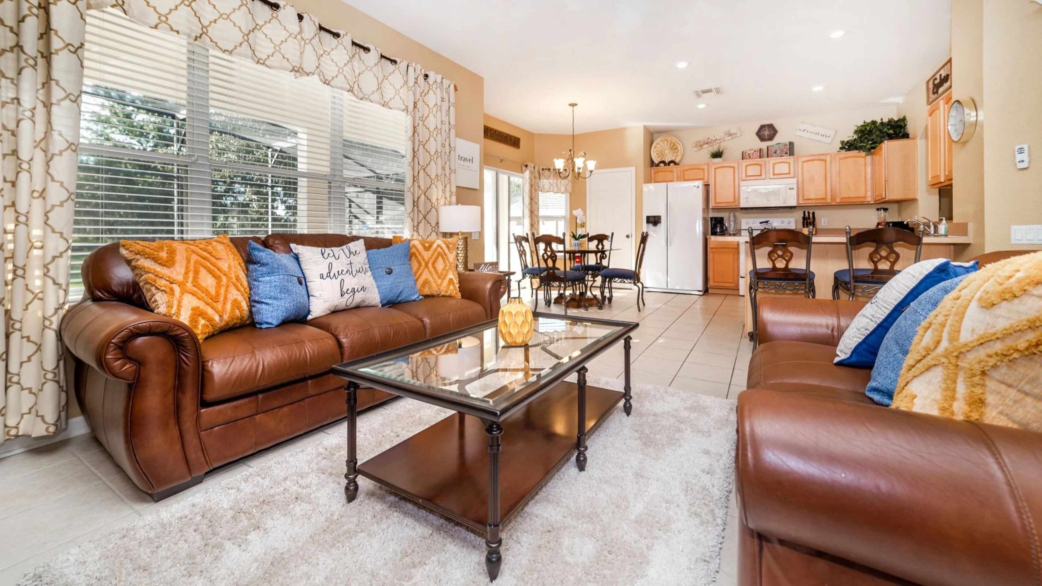 A living room with a brown leather sofa, a glass coffee table, and a dining area with wooden chairs.