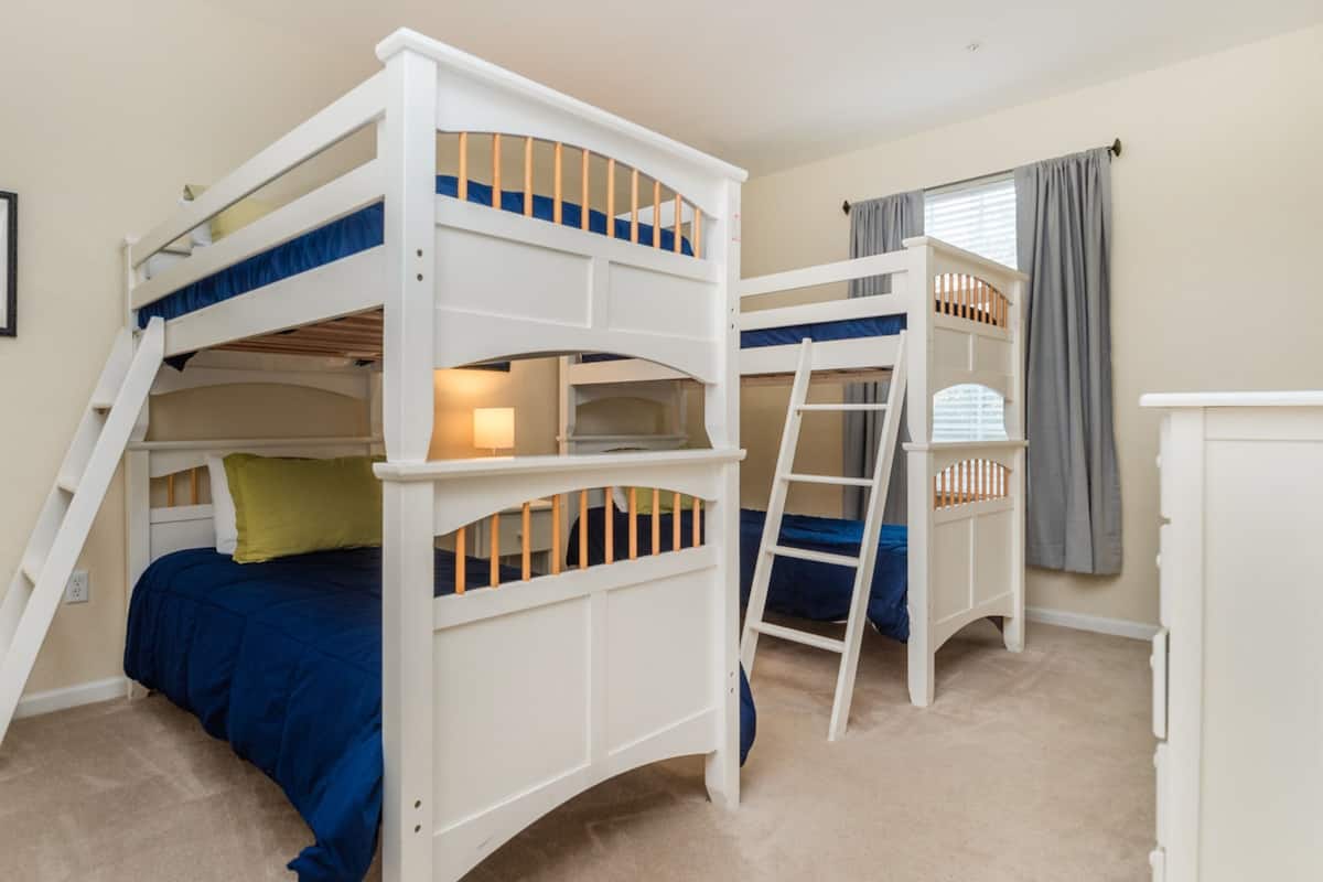 A bunk bed room with a ladder, a desk, and a window with curtains.