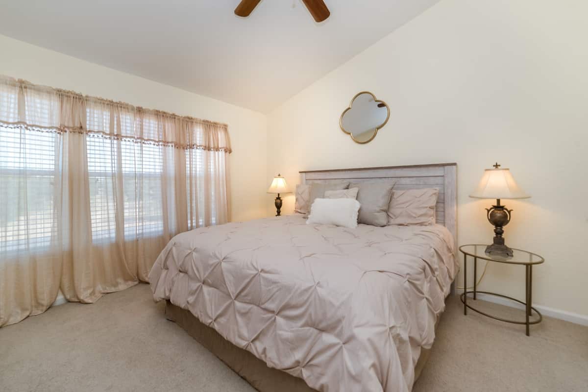 A bedroom with a large bed, two bedside lamps, a mirror, and sheer curtains.