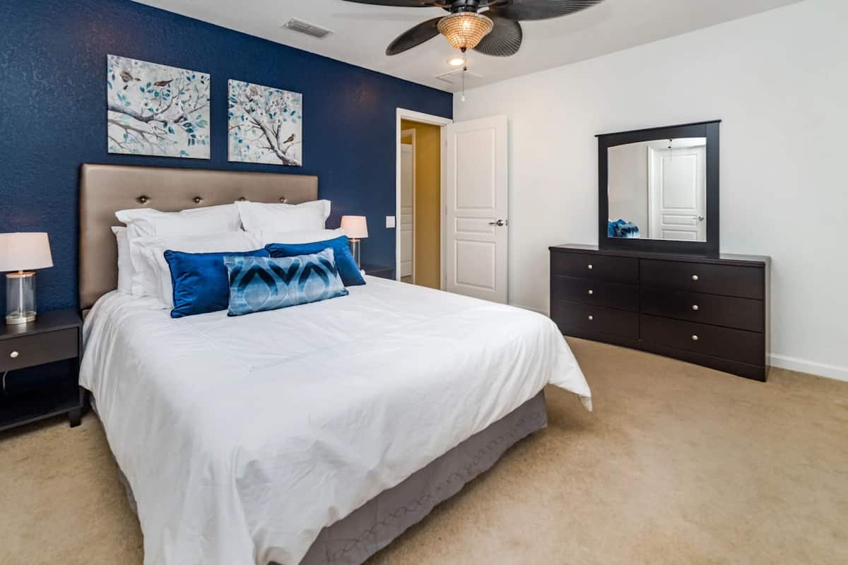 A bedroom with a bed, nightstands, a dresser, a ceiling fan, and artwork on the wall.