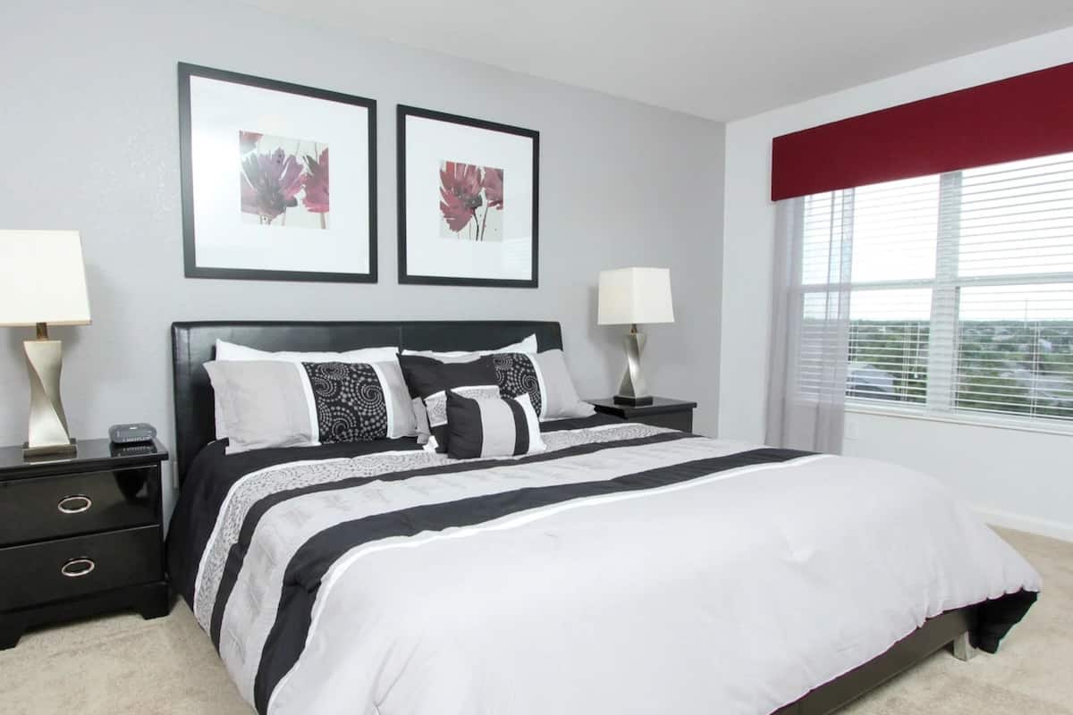 A bedroom with a large bed, two nightstands, a window with blinds, and two framed pictures on the wall.