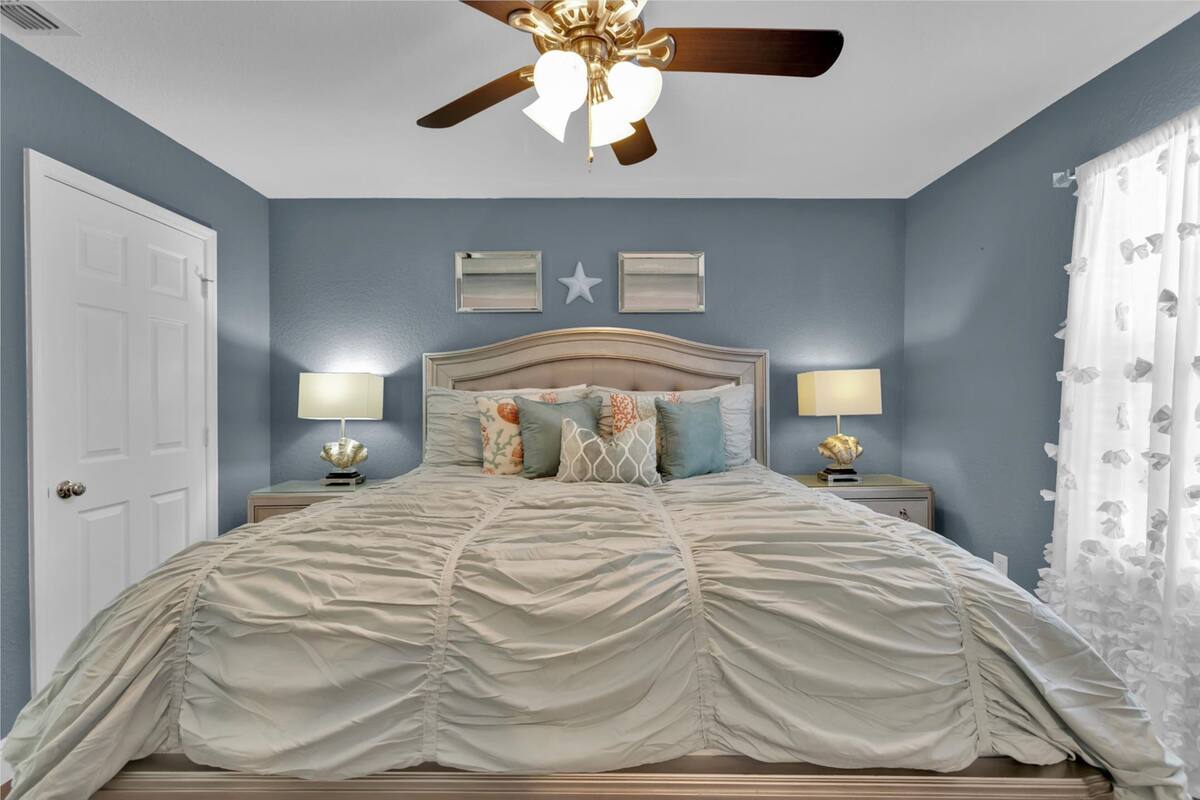 A bedroom with a bed, two bedside tables with lamps, a ceiling fan, and a door.