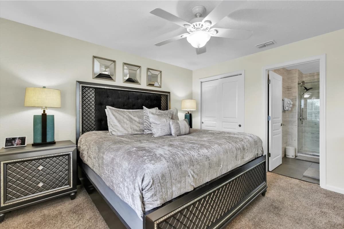 A bedroom with a bed, two bedside tables, a ceiling fan, and a door leading to a bathroom.