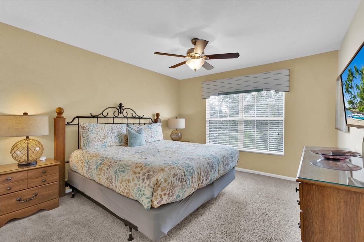 A bedroom with a bed, a nightstand, a dresser, a ceiling fan, and a window with blinds.