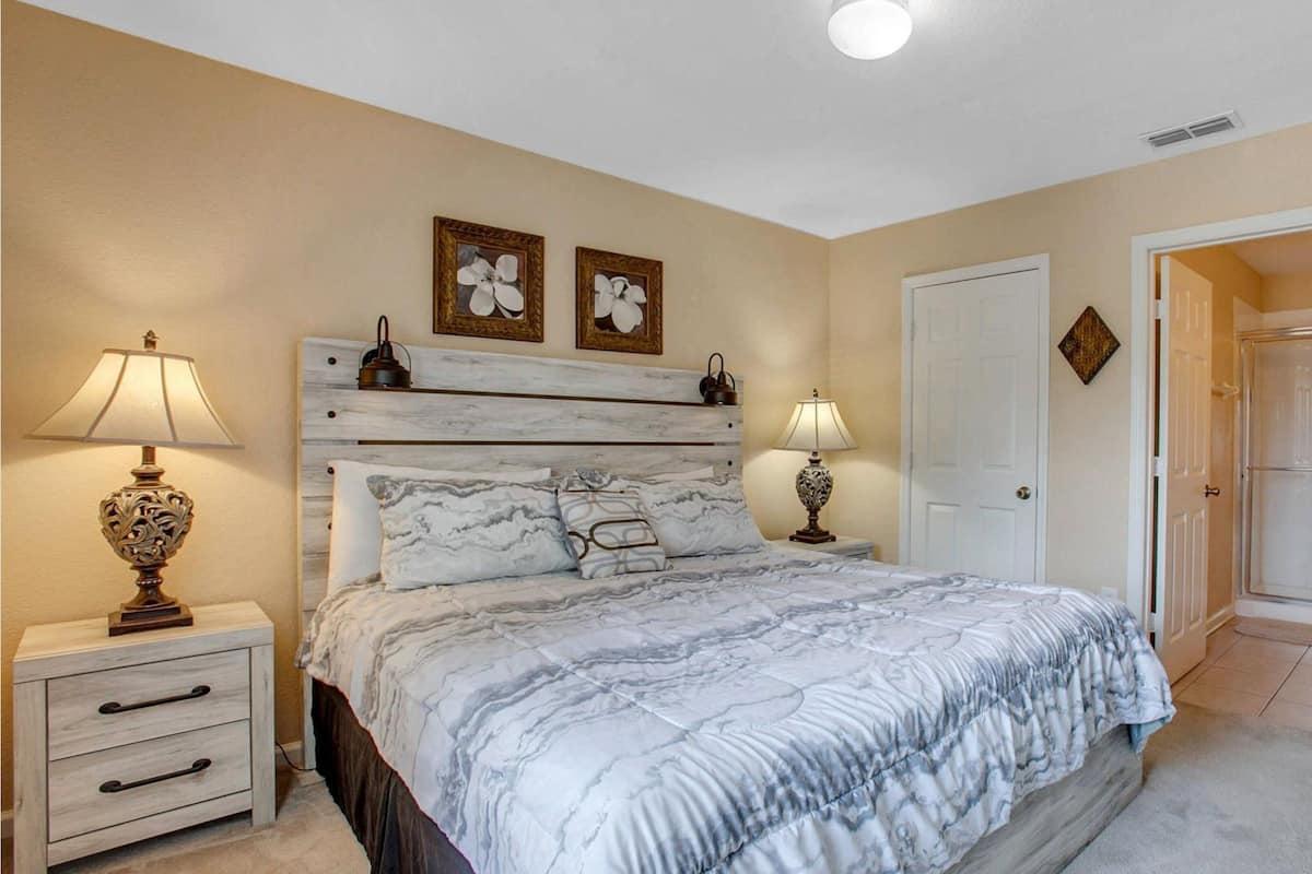 A bedroom with a bed, two bedside tables, two lamps, a door, and a small plant.