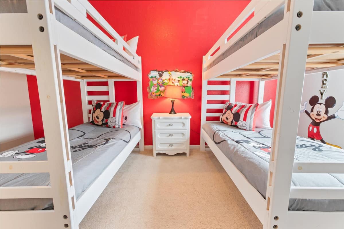 A room with bunk beds, a nightstand, a lamp, and a wall decoration.