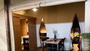 Quarto compacto com piso de madeira, uma mesa de jantar com cadeiras e uma pequena cozinha no fundo.