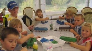 Um grupo de crianças participando de uma atividade artística em uma mesa com materiais de arte.