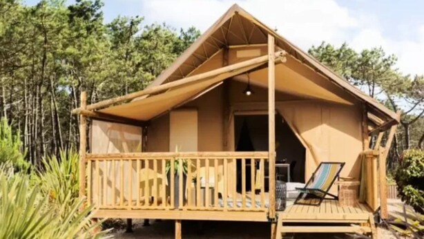 Uma cabana de madeira com varanda, uma cama de solteiro e uma pequena mesa.