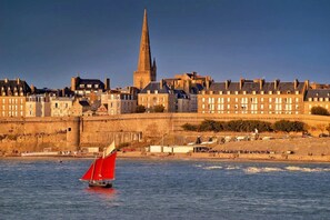 A coastal cityscape with a prominent tower and a red sailboat on the water. - ZEcamping 1* locatif BBQ 27m2 2 pers (Saint-Benoît-des-Ondes)