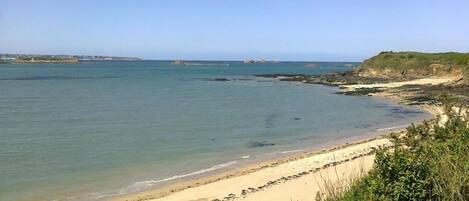 A coastal beach with clear waters, rocky outcrops, and a distant shoreline.