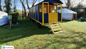 Une petite cabane d’une seule pièce, dotée d’une rampe menant à l’entrée, et entourée d’arbres et d’herbe.