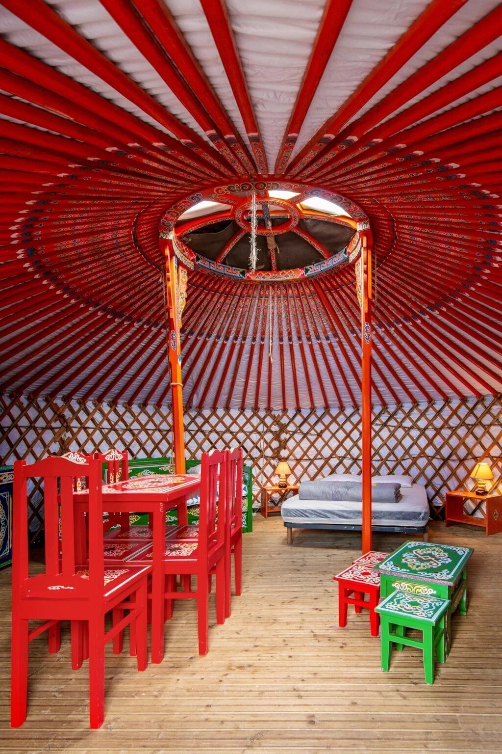 A traditional yurt with a central wooden structure, a bed, and a dining area with chairs and tables.
