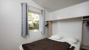Een kleine kamer met een enkel bed, een raam, een kast en een bed met een bruine deken.