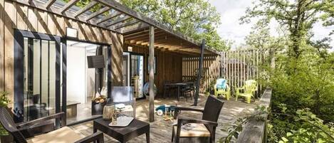 A covered outdoor patio with wooden flooring, a table, chairs, and a seating area with cushions.