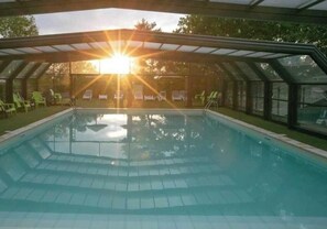 A swimming pool with a covered area, surrounded by green chairs, under a glass roof.