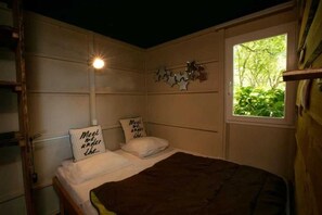 A bedroom with a bed, two pillows with text, a wall-mounted light, and a window with greenery outside.