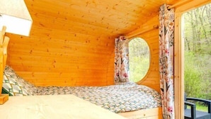 A wooden cabin room with a bed, a window with curtains, and a view of the outdoors.