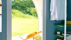 A room with a wooden chair, a white towel hanging on a rack, and a view of greenery outside. - ZEcamping 3* piscine chauffée pet friendly sauna roulotte 11m2 2 pers (Huelgoat)