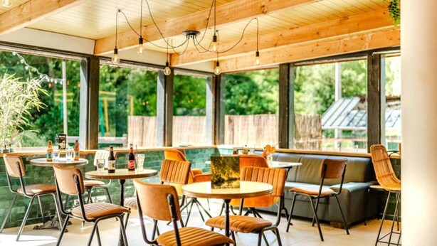 Un vaste espace extérieur aménagé pour les repas, avec des poutres en bois, des tables rondes et des sièges confortables.