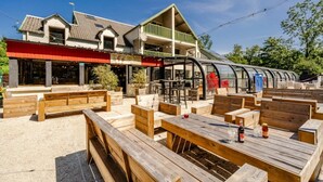 Un espace extérieur aménagé avec des bancs et des tables en bois, une terrasse couverte et un bâtiment doté d’un toit végétalisé et d’une marquise rouge.