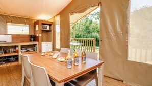 A tented accommodation with a wooden dining table, chairs, a microwave, and a small kitchen area. - ZEcamping 3 étoiles piscine chauffée jacuzzi sauna tente 5 pers (Huelgoat)