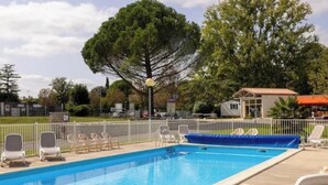 A rectangular swimming pool with a blue interior, surrounded by white lounge chairs and a white fence. - ZEcamping 3 étoiles piscine locatif 4 pers (Saintes)