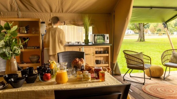 A tented dining area with a table set for breakfast, a kitchen area, and a view of the outdoors. - ZEcamping 3 étoiles piscine locatif 4 pers (Saintes)