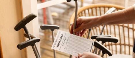 Een persoon houdt een golfscorekaart met de tekst 'MINI-GOLF' vast, in de buurt van een golfkar.