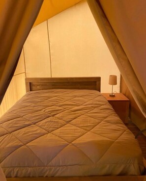 Ein Zeltraum mit Bett, Nachttisch und Lampe.