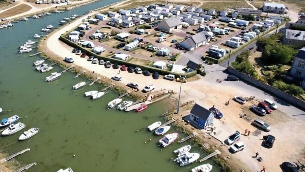 Vista aérea de un puerto deportivo con barcos amarrados, una playa de arena y una hilera de edificios.