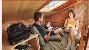 A small, wooden cabin with a skylight, a bed with pillows, and a backpack on a shelf. - ZEcamping 3 étoiles toboggans dog friendly locatif 5m2 4 pers (Quinéville)
