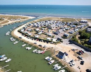 An aerial view of a marina with boats docked, a sandy beach, and a row of buildings.