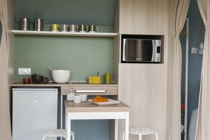 A compact kitchenette with a microwave, a small fridge, a white table, and stools. - ZEcamping 3* piscine dog friendly bien-être locatif 16m2 4 pers (Urt)