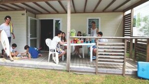 Un espacio al aire libre cubierto con una mesa y sillas, un pequeño jardín y un edificio con puerta y ventanas.