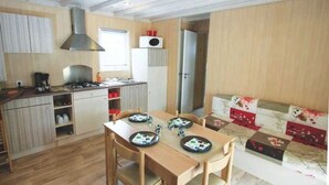 Una cocina compacta con estufa, lavabo y armarios, una mesa de comedor con sillas, y un sofá con cojines estampados.