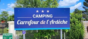 Un senyal blau amb la inscripció 'CAMPING Carrefour de l'Ardèche' i tres estrelles a sobre.