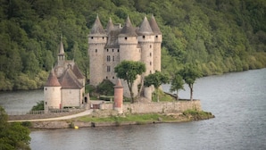Eine Burg mit mehreren Türmen, einem Burggraben und einem Fluss im Hintergrund.