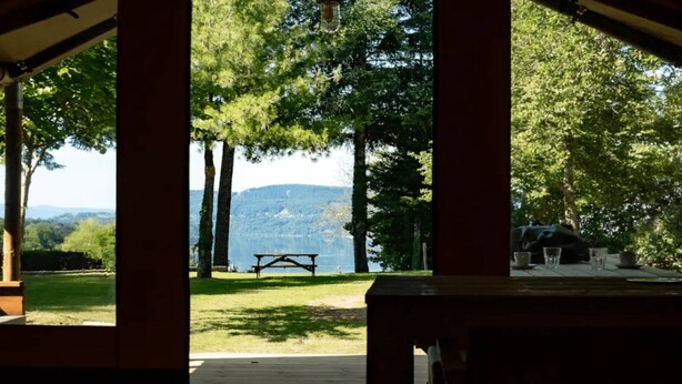Eine Holzterrasse mit Picknicktisch und Gläsern, mit Blick auf einen See und Berge.