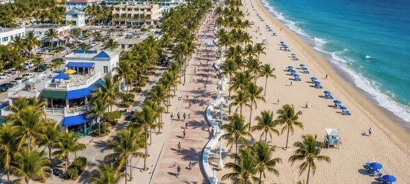 A coastal hotel with a beach promenade lined with palm trees, a sandy beach with umbrellas, and ocean views. - Tropical Getaway~Heated Pool~MiniGolf~BBQ~Pool table~Near FIFA World Cup Stadium (Fort Lauderdale)