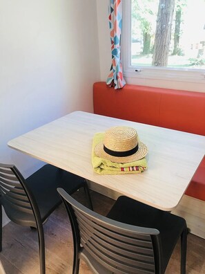 A table with a woven hat and a towel, two chairs, a window with a curtain, and a red bench. - ZEcamping 4* piscine club enfant - mobil-home 18m2 sanitaires communs (Proissans)