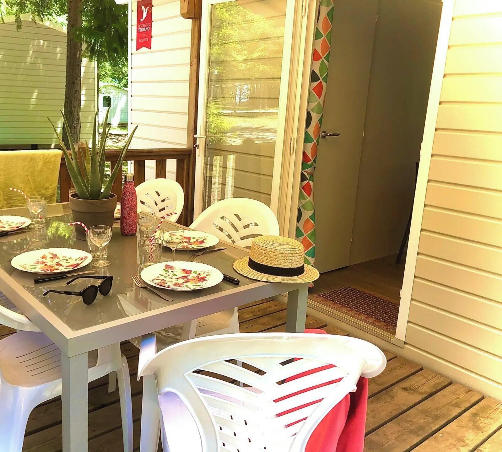 A dining table set with plates, glasses, and a hat, surrounded by white chairs.