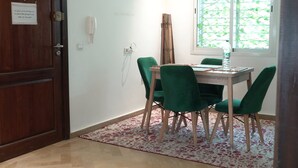 Ein Zimmer mit Holztür, Tisch mit grünen Stühlen, Fenster mit Blick auf Bäume und einem gemusterten Teppich.