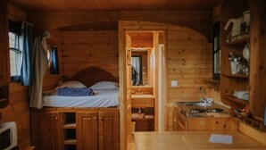 Indretning i en hyggelig hytte med seng, træskabe, vask og et vindue med gardiner.