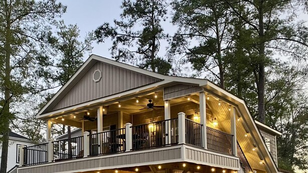 Een huis met twee verdiepingen, voorzien van een balkon, houten terras en buitenverlichting.