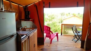 A kitchen with a refrigerator, a sink, and a coffee maker. There is a wooden deck with a red chair and a table. - ZEcamping 3* pataugeoire piscine locatif 20m2 5 pers (Saint-Mitre-les-Remparts)