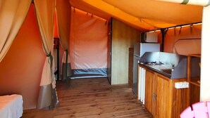 A tented accommodation with a wooden floor, a kitchenette with a stove, and a bed. - ZEcamping 3* pataugeoire piscine locatif 20m2 5 pers (Saint-Mitre-les-Remparts)