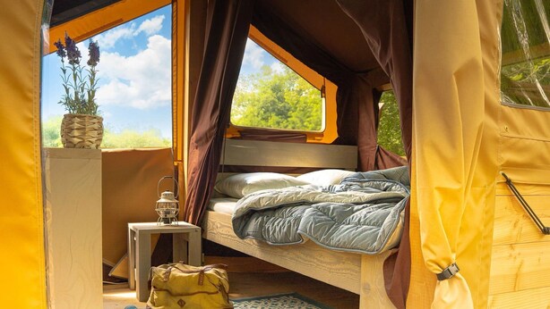 A tent interior with a bed, a lantern, and a bag.
